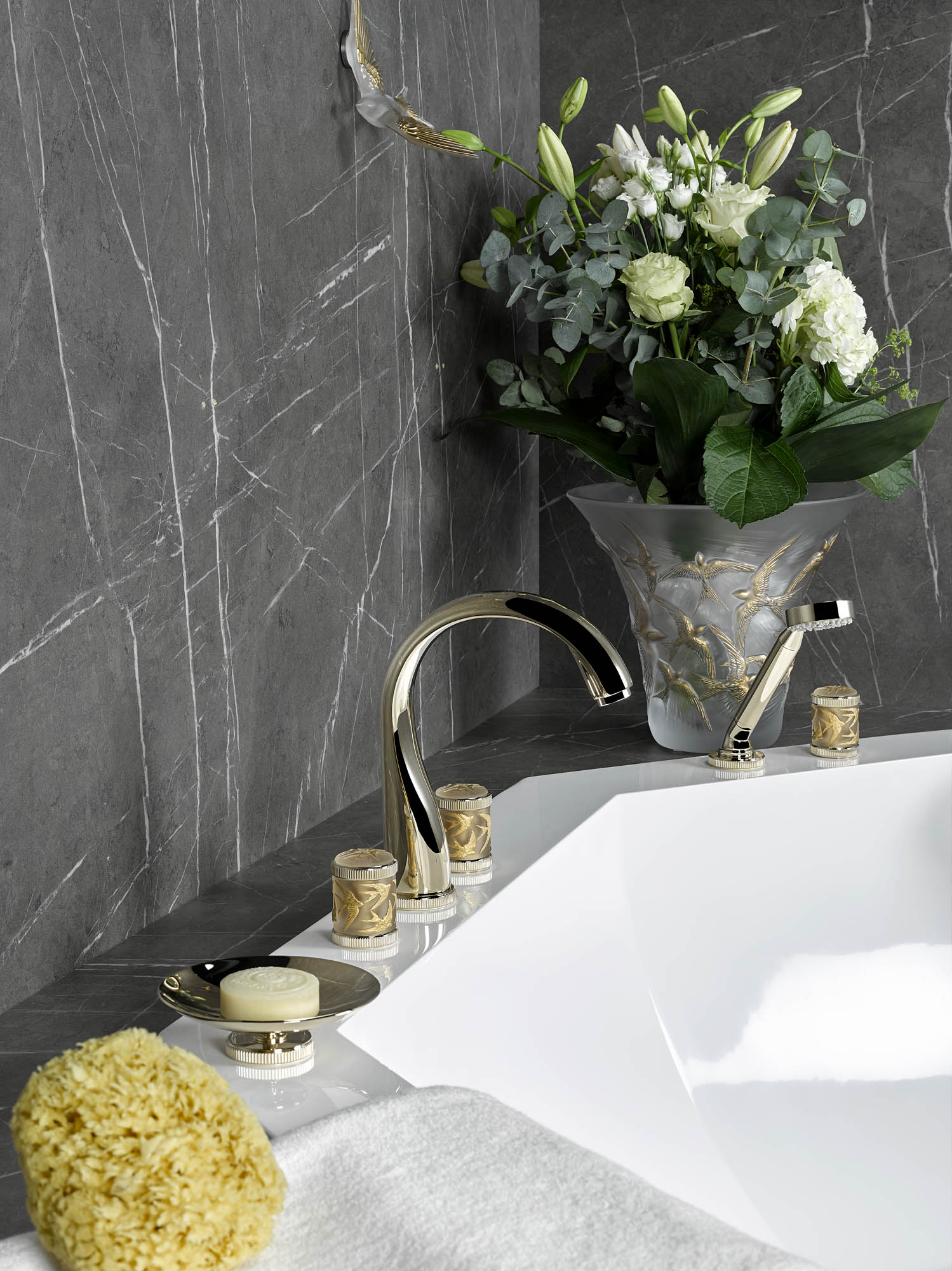 a close-up of a tub with gold faucet and décor surrounding it including soap, a loofah and a vase of flowers