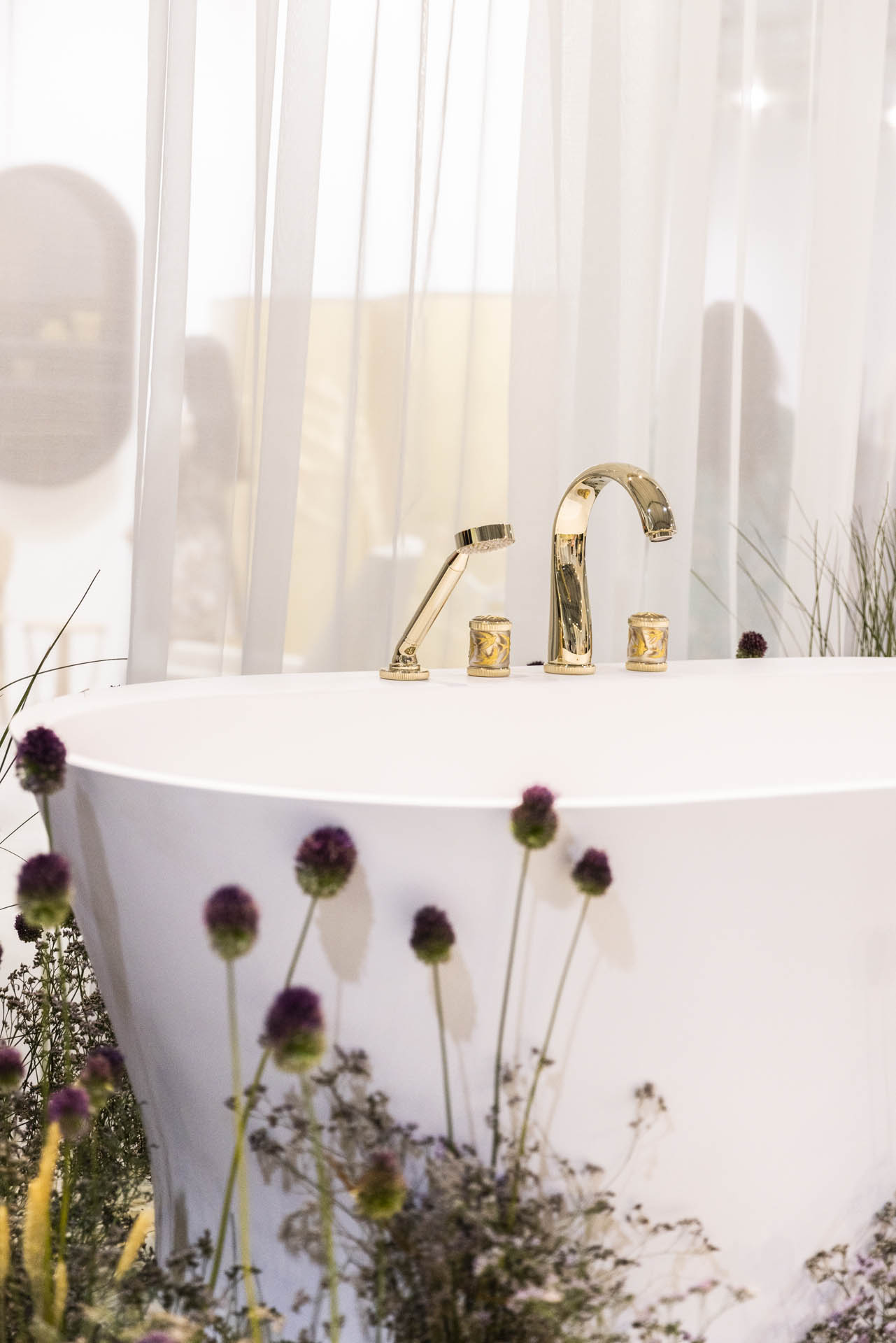 a tub with gold faucet surrounding by plants 