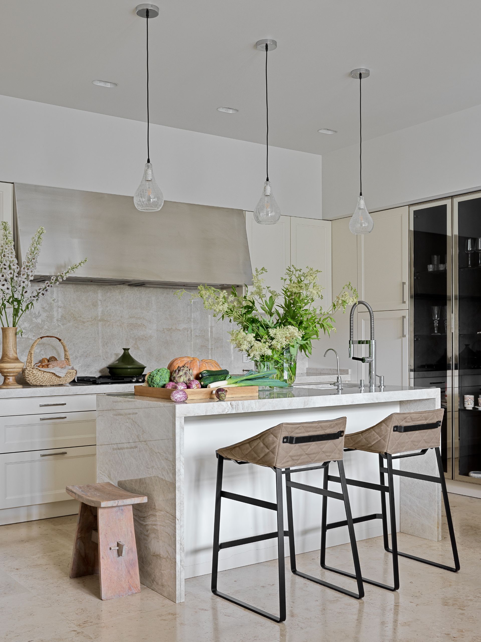 Kitchen custom made by Fiberwood featuring Taj Mahal marble, Venezia Stone, Piet Boon bar stools and Oly Studio lighting. 