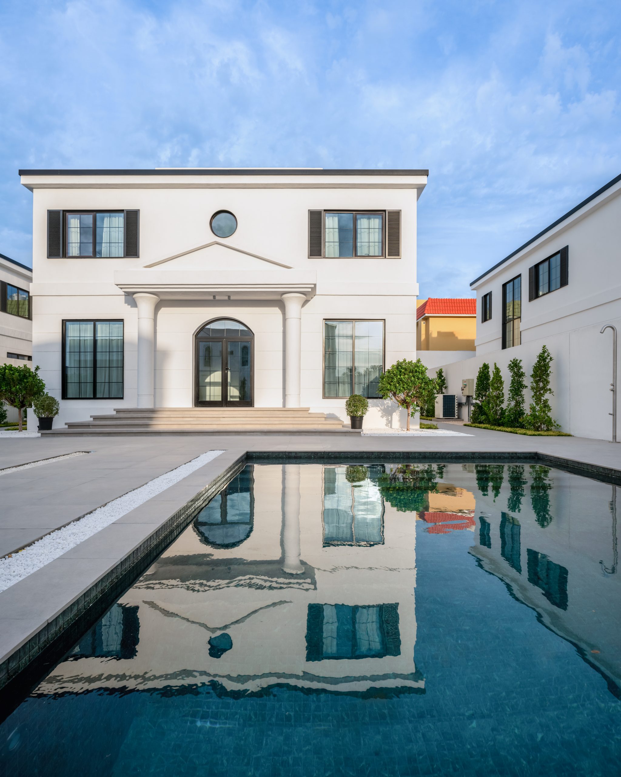 the exterior of the home with a pool and a more square shaped home with door that has a semicircular top and rectangle doors. the main door is placed between two pillars