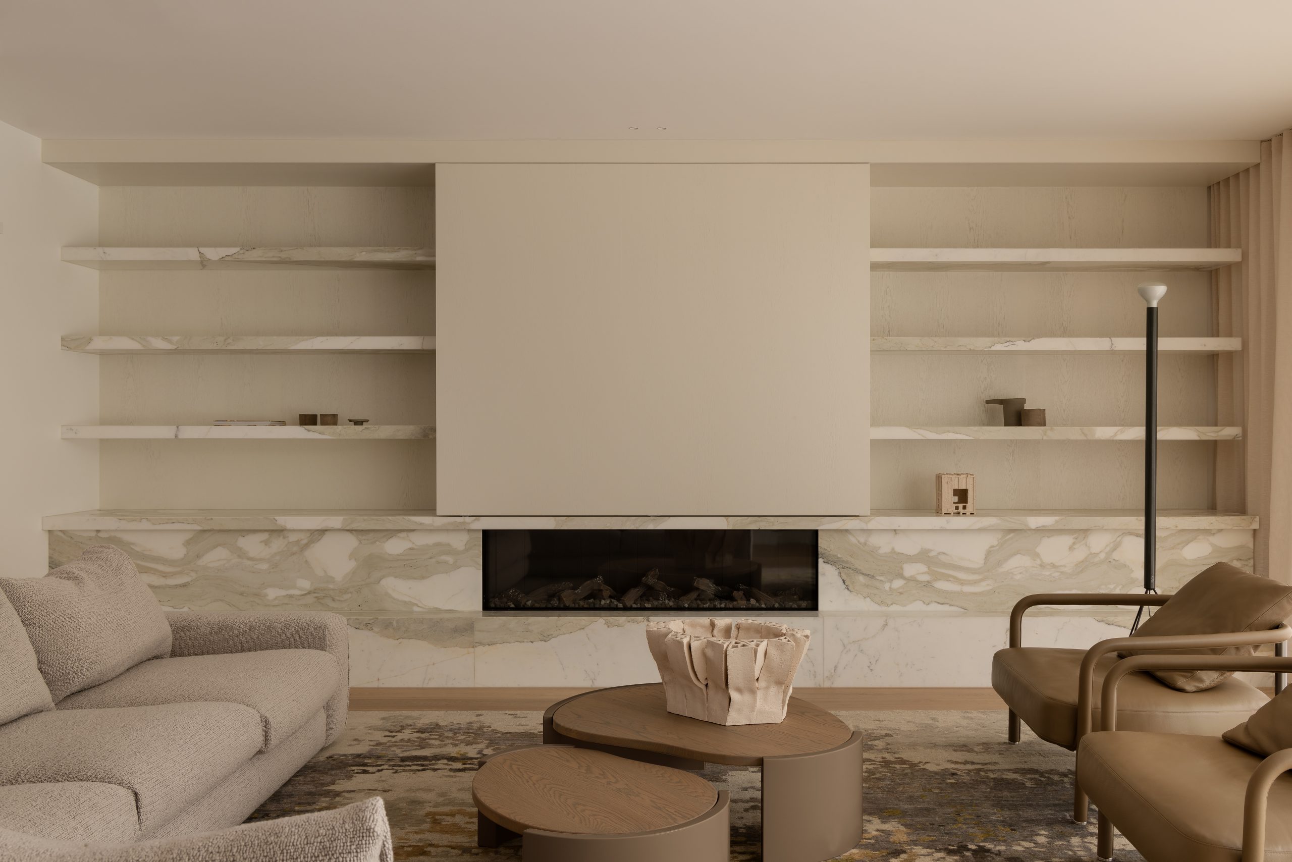 Full view of the TV Room decorated in marble finishing, with unique furniture designed by Homeroom studio, that includes a centerpiece placed between a wrap around couch and two armchairs.