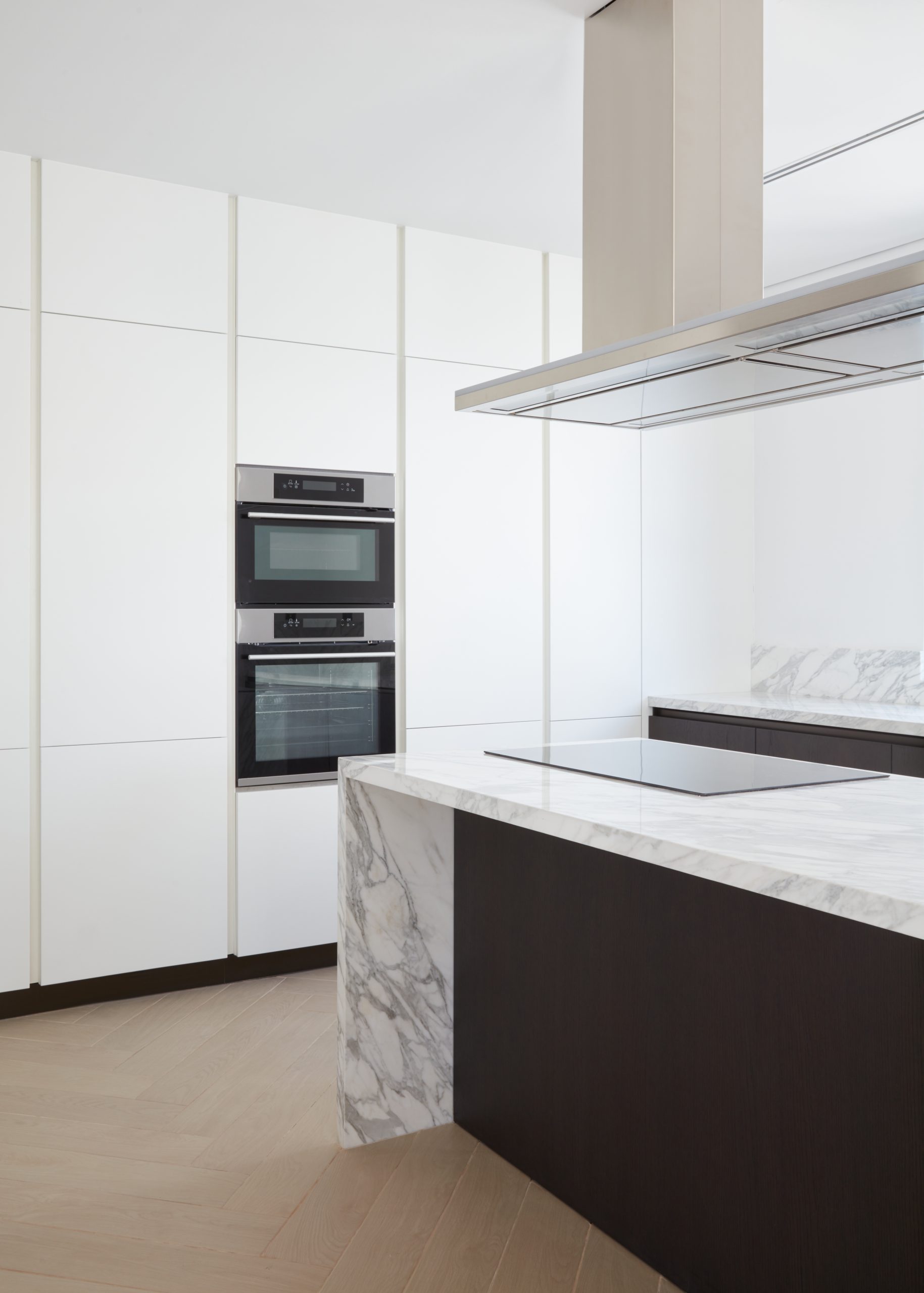 The sleek modern kitchen with white cabinets and embedded oven and microwave. There is marble countertops with black finishing's