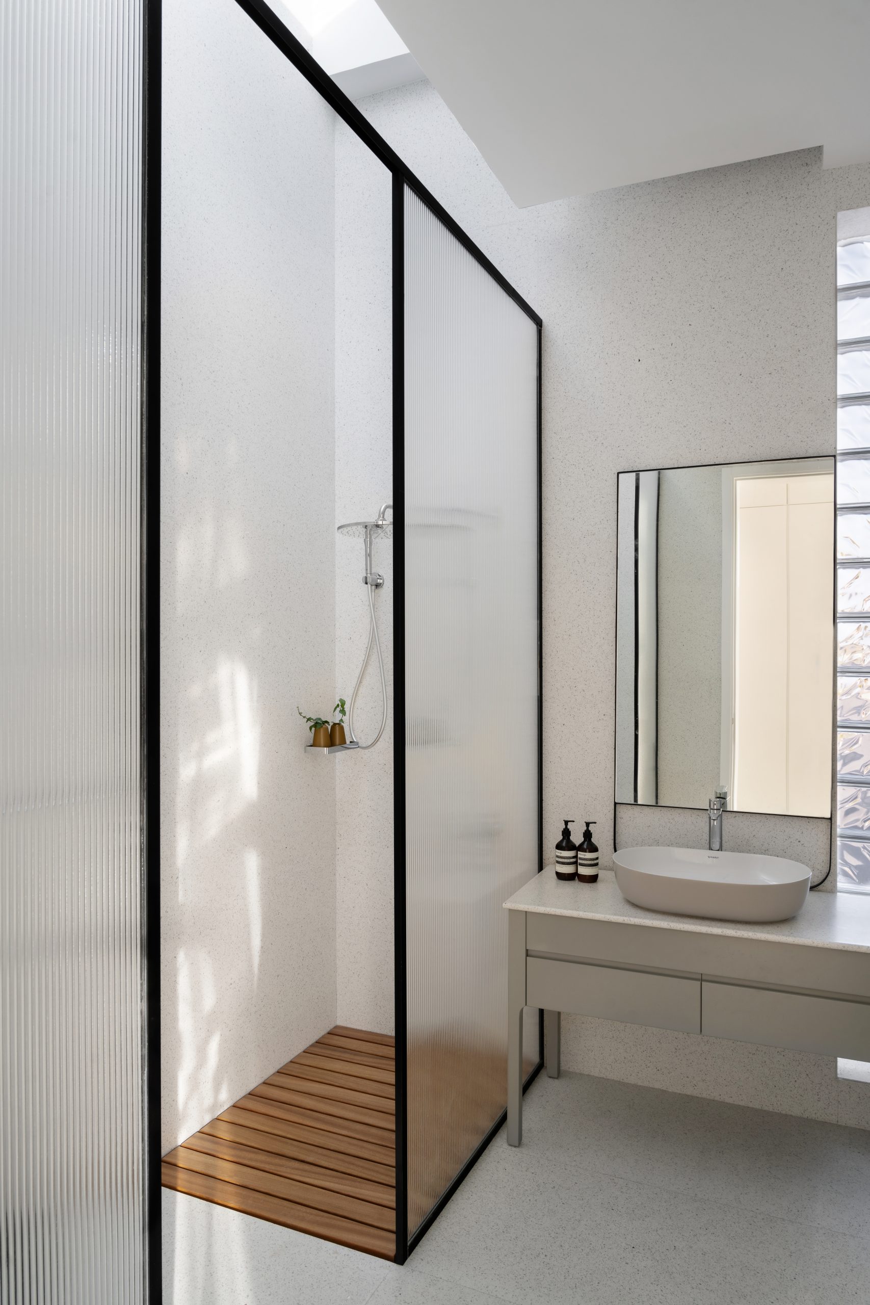 a bathroom with a standing shower with a wooden floor and black outlined glass