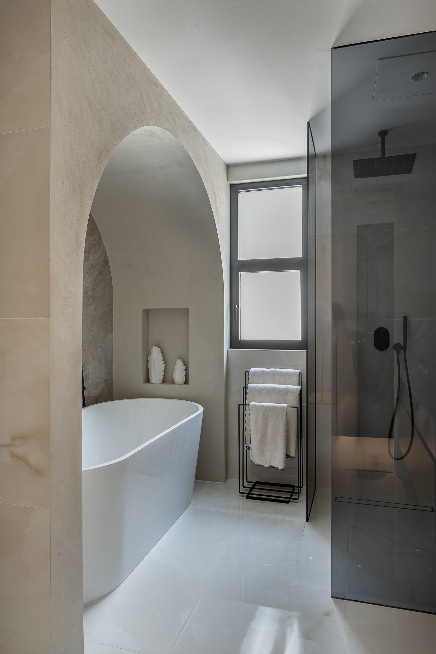 master bedroom bathroom with a clean aesthetic look, a bathtub placed under an arch and a stand shower