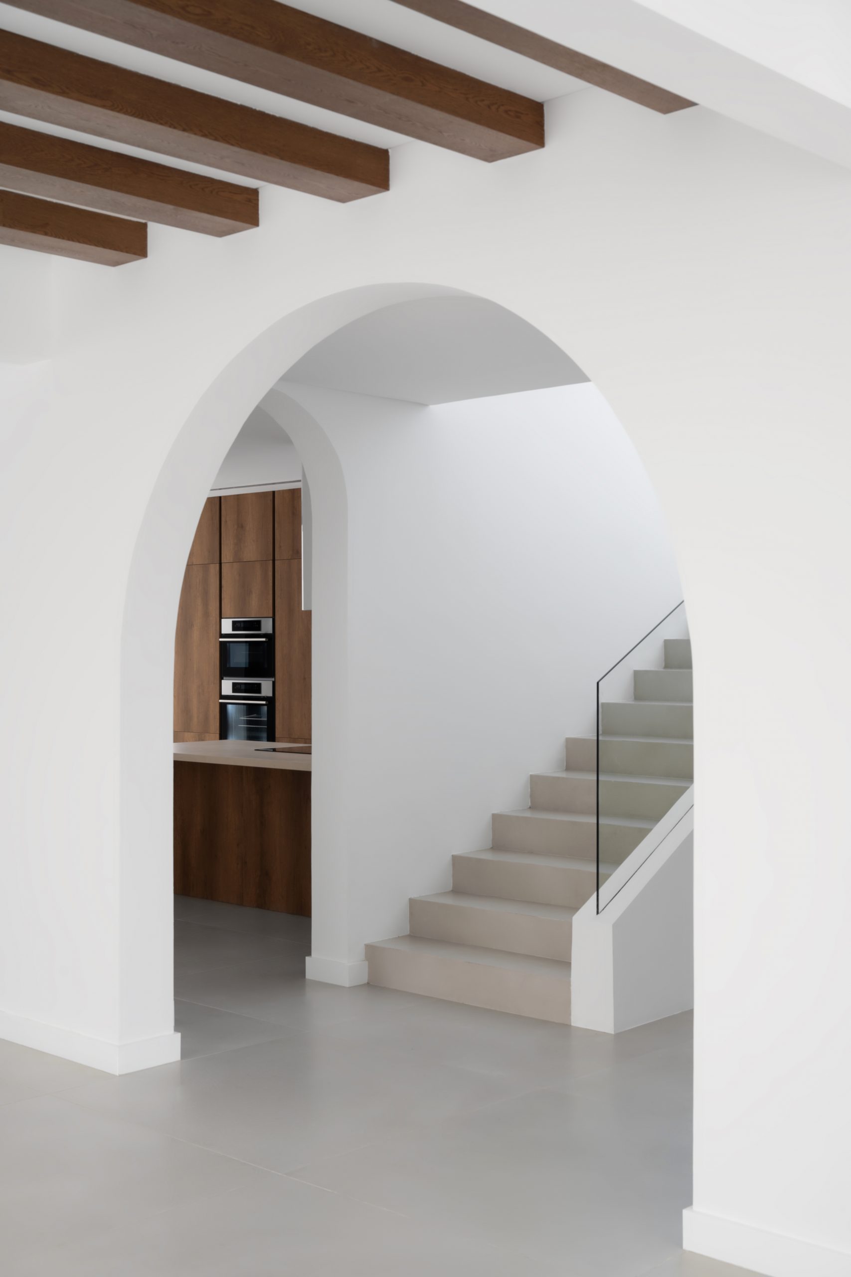 Next to the staircase there is a kitchen on the left and a beautiful arch entryway right before the staircase with wooden fixtures on the ceiling